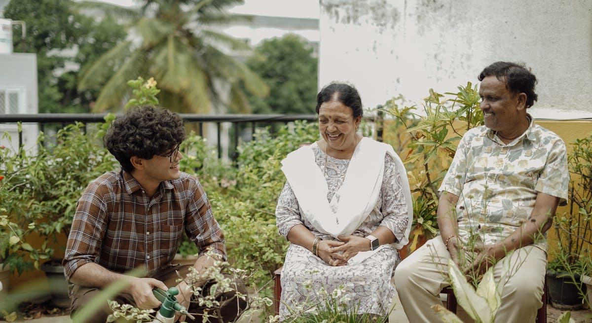 A Concierge sitting with an elder couple among the plants on their terrace